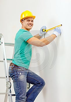 Smiling man in protective helmet measuring wall