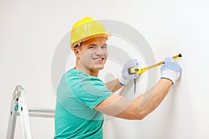 Smiling man in protective helmet measuring wall