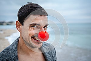 Smiling man with a red nose on the beach in morning hangover.