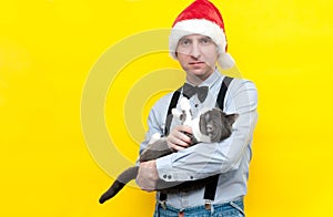 Smiling man in red santa hat, blue shirt and black suspender holding cute grey cat and looking at camera