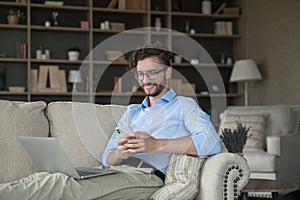 Smiling man rest on sofa with laptop and smartphone