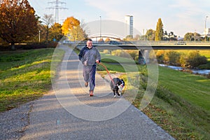 Smiling man running his dog along a footpath at sunset