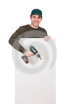 Smiling man with a screwdriver or electric drill in his hand, stands behind a white panel. Renovation worker before installing