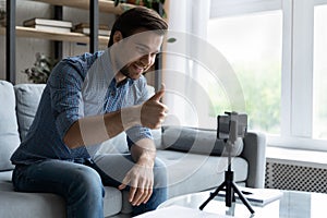 Smiling man showing thumb up, using smartphone on tripod