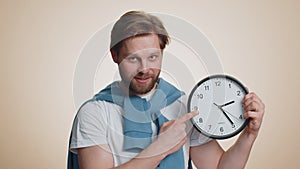 Smiling man showing time on wall office clock, ok, thumb up, approve, pointing finger at camera