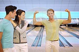 Smiling man shows arm muscles; pair look at him
