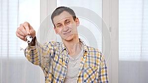Smiling man shows keys with house breloque near window
