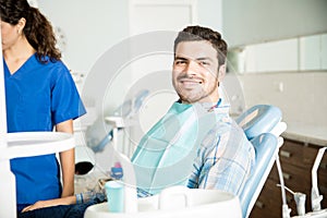 Smiling Man Sitting On Chair While Dentist Working In Clinic