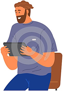 Smiling man sitting on chair holds tablet. Guy uses gadget to chat, surf internet and watch video