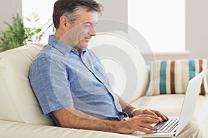 Smiling man sitting on a sofa using a laptop