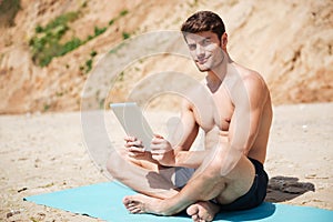 Smiling man sitting and using tablet on the beach