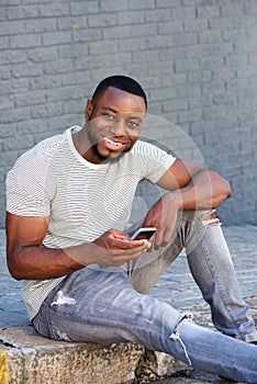 Smiling man with smart phone sitting on curb outside