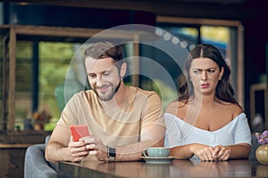 Smiling man with smartphone and angry woman