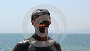 Smiling man smeared with mud, visible minor patches of skin. Dead Sea. Jordan