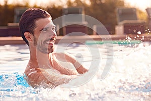 Smiling Man Splashing Water On Summer Vacation In Outdoor Swimming Pool