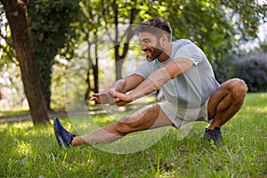 Smiling man in sportswear is doing warming up before running in the city parkland