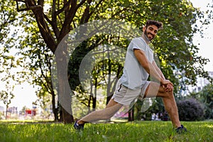 Smiling man in sportswear is doing warming up before running in the city parkland and looks camera