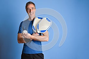 Smiling man in sportswear with pickleball equipment blue isolated background