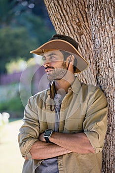 Smiling man standing with arms crossed near tree trunk
