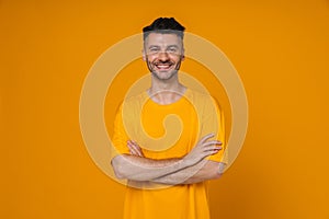 Smiling man standing with arms folded isolated over yellow wall