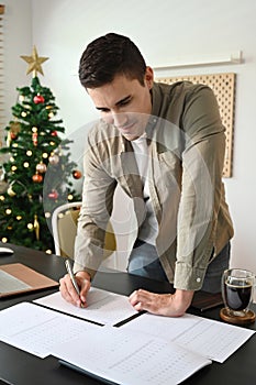 Man standing in home office and checking reports on wooden table.