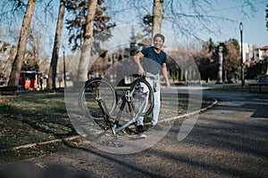 Smiling man standing next to an overturned bicycle in a sunny park setting