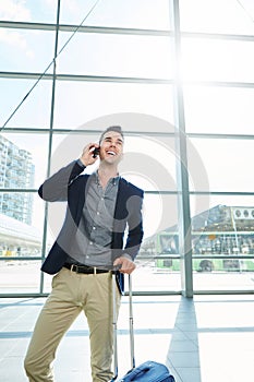 Smiling man standing in station with mobile phone and suitcase