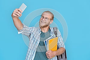 Smiling man student blogger hold phone record vlog isolated on blue background.