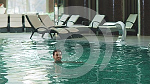 Smiling man swimming at modern hotel. Sexy guy bathing at luxury pool indoor.
