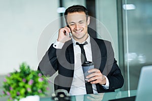 Smiling man talking on mobile phone while using laptop computer at desk