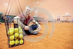 Smiling man tennis trainer player with racket and ball on court