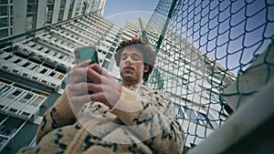 Smiling man texting cellphone at urban buildings backdrop closeup bottom view.