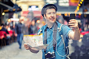 Smiling man tourist in London taking a selfie on crowded streets full of pubs, Happy middle aged male holding city map vlogging photo