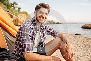 Smiling man tourist sitting in touristic tent at the beach