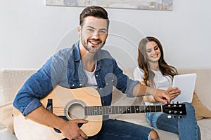 smiling man tuning guitar and looking at camera while his girlfriend