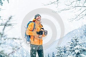 Man with a hot drink cup and a thermos flask dressed bright orange softshell jacket drinking while he trekking winter mountains