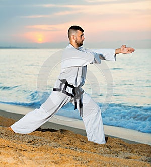 Man in uniform doing taekwondo exercises at sunset sea shore