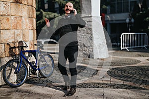 Smiling man on urban background taking a break with his bicycle and making a phone call.