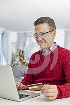 Smiling man using credit card and laptop to shop online at home during Christmas