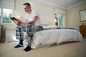 Man using digital tablet on bed in bedroom