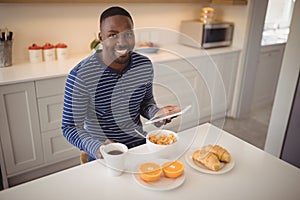 Smiling man using a digital tablet while having breakfast in kitchen