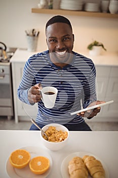 Smiling man using a digital tablet while having cup of coffee in kitchen