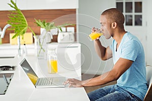 Smiling man using laptop and drinking orange juice