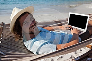 Smiling man using laptop while relaxing on hammock in beach