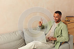 Smiling Man Using Laptop At Sofa. Guy Relaxing With Laptop At Home On Cozy Couch