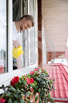 Smiling man watering flowers in outdoor flower pot in country house, home owner