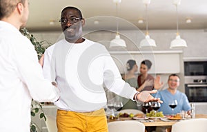 Smiling man welcoming friend to dinner party with handshake