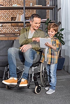 smiling man in wheelchair and little son using tablet together