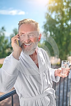 Smiling man in the white bathrobe making a phone call