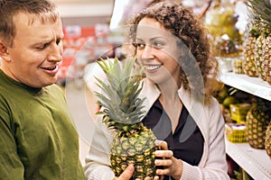 Smiling man and woman buy pineapple in supermarket